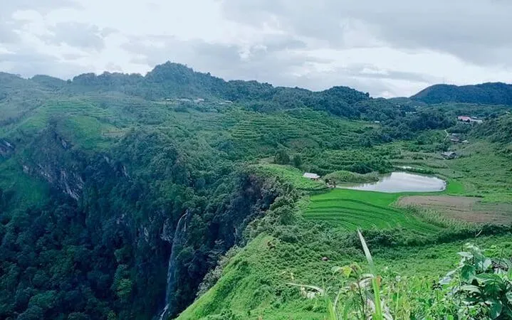 Lush green terraces and hills in Sapa, Vietnam, with a distant waterfall and tea farm.