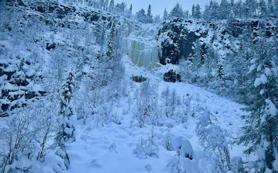 Korouoma Canyon's frozen waterfall surrounded by snow-covered trees, Rovaniemi.