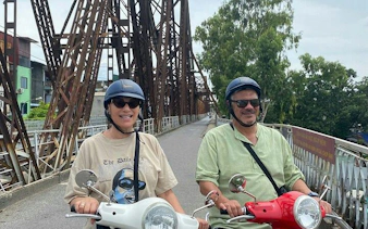 Tourists riding Vespas on Long Bien Bridge during Hanoi countryside tour to Bat Trang Ceramic Village.