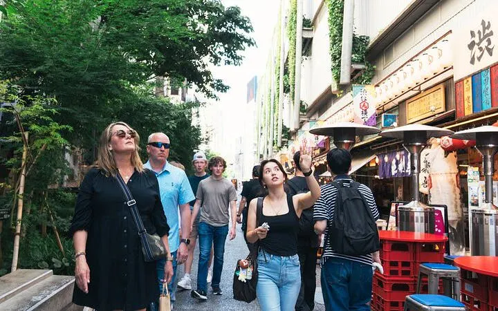 Tourists exploring Shibuya street with guide pointing at local shops, Tokyo.