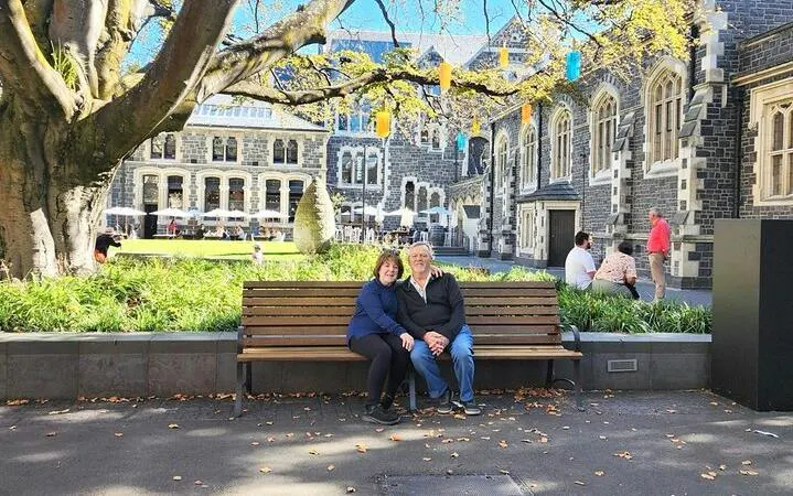 Christchurch city tour with visitors sitting on a bench in front of historic stone building.