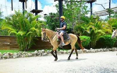 Horseback rider on Punta Cana tour path with lush greenery and adventure park backdrop.