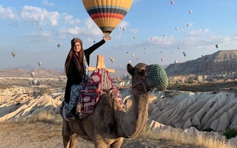 Camel ride in Cappadocia with hot air balloons at sunrise in the background.