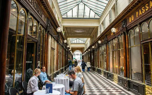 Parisian covered passageway with people dining and walking, part of a 2-hour walking tour.