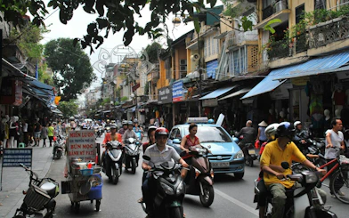 Scooters and cars navigate a busy street in Hanoi Old Quarter, Vietnam.