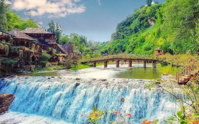 Waterfall and wooden bridge in lush Sapa village landscape, Vietnam.