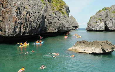 Kayakers and snorkelers explore Ang Thong National Marine Park's clear waters near rocky cliffs, Koh Samui.