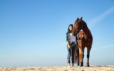 Person standing with a horse on a sandy beach under a clear blue sky in Hurghada.
