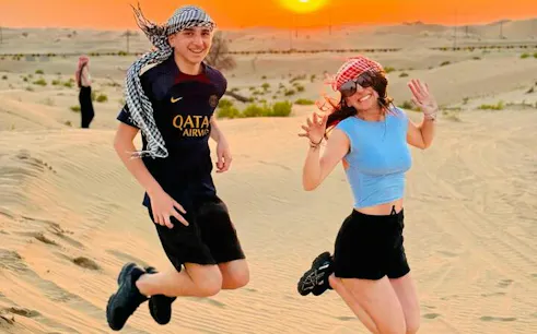 Jumping tourists in Abu Dhabi desert at sunset during safari tour.