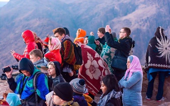 Tourists wrapped in blankets watching sunrise on Moses Mountain during Saint Catherine Monastery tour.