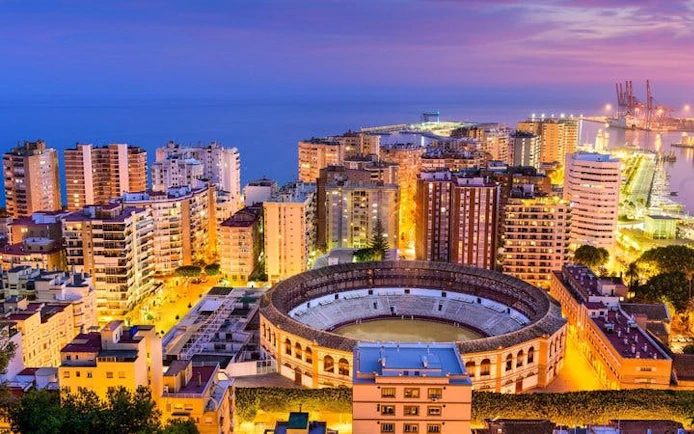 Malaga cityscape with bullring and harbor at dusk, view from above.