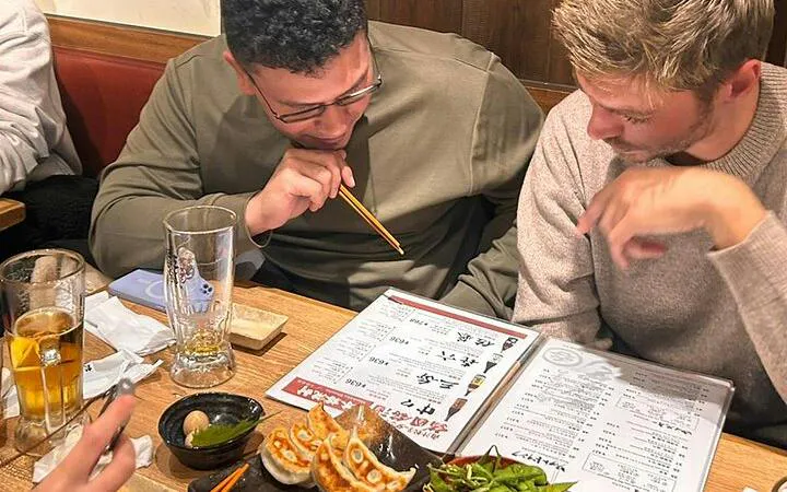 Two people examining a menu at a Tokyo eatery with gyoza and drinks on the table.