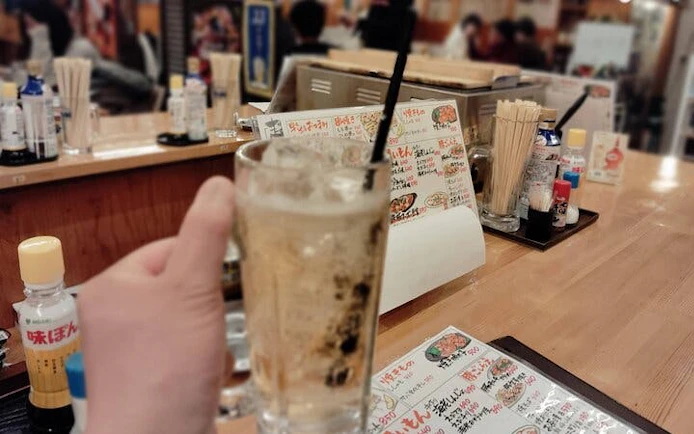 Hand holding a drink at a Nakasu food stall in Fukuoka with menu in background.