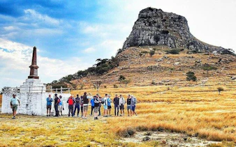 Group touring Isandlwana battlefield monument, KwaZulu-Natal, with mountain backdrop.