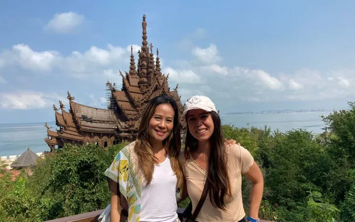 Two visitors at the Sanctuary of Truth in Pattaya with ocean view in the background.