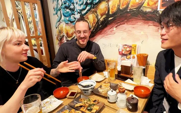 Group enjoying food and drinks at a lively bar in Shinjuku, Tokyo during a night walking tour.