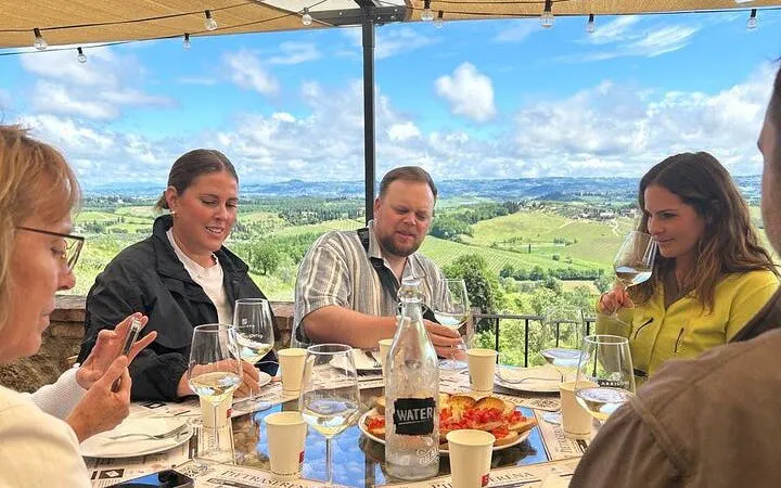 Group enjoying wine tasting at a Chianti winery with view of San Gimignano countryside.