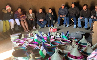 Tourists seated in a Lesotho hut with traditional baskets and flags during Sani Pass tour from Durban.