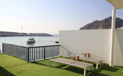 Boat docked by a waterfront terrace in Fujairah with mountain view.