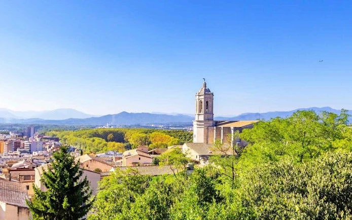 Girona cityscape with Cathedral of Girona tower and surrounding greenery.