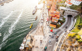 Aerial view of Porto riverside promenade with tourists, colorful buildings, and boats on the Douro River.