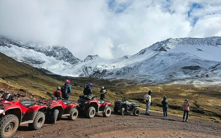 ATVs parked with tourists viewing snow-capped mountains on Rainbow Mountain tour, Cusco.