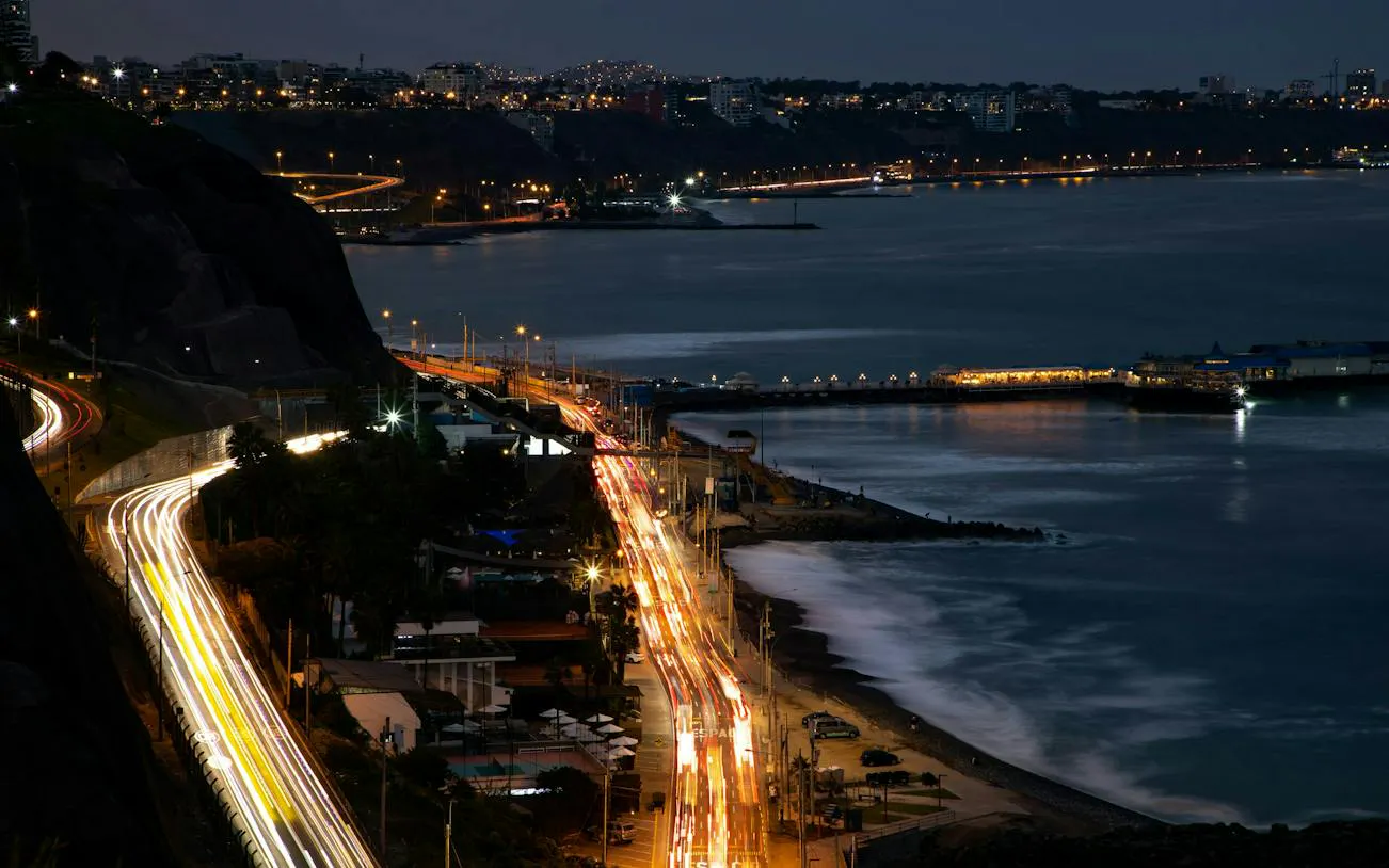 Night view of Lima's Barranco district coastline with illuminated roads and city lights.
