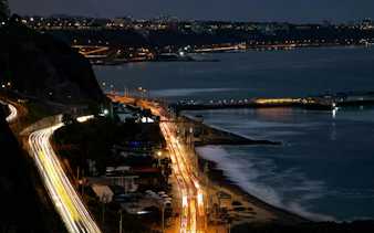 Night view of Lima's Barranco district coastline with illuminated roads and city lights.
