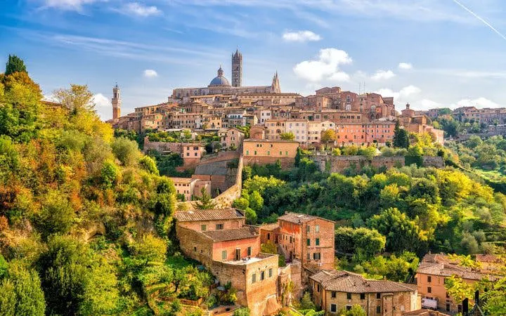 Siena cityscape with historic buildings and cathedral, view from a hill, Italy.
