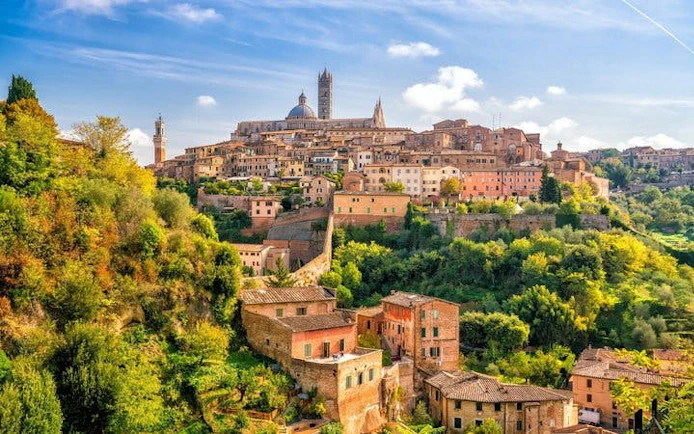 Siena cityscape with historic buildings and cathedral, view from a hill, Italy.