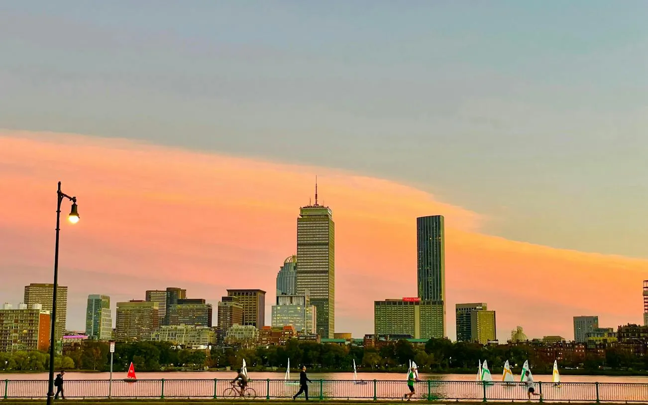 Boston skyline at sunset with Charles River and sailboats, viewed from Harvard Bridge.