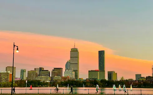 Boston skyline at sunset with Charles River and sailboats, viewed from Harvard Bridge.