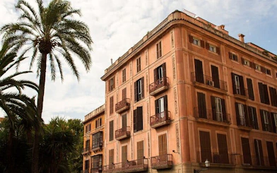 Historic building with shutters and balconies in Palma de Mallorca, framed by palm trees.