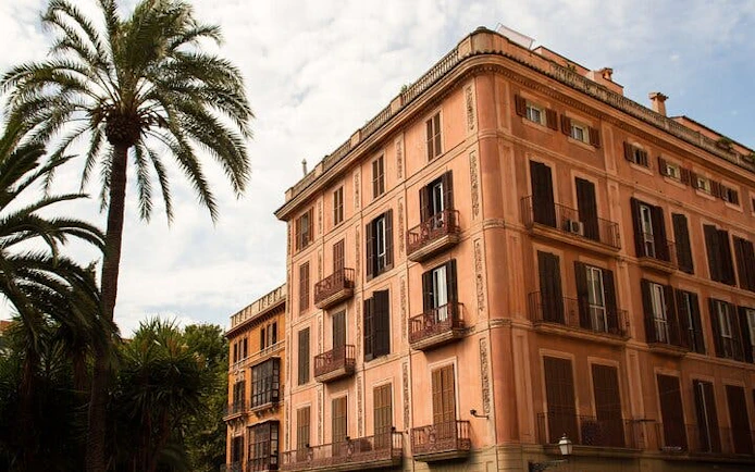 Historic building with shutters and balconies in Palma de Mallorca, framed by palm trees.