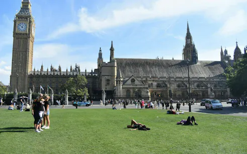 Westminster Abbey and Big Ben with people relaxing on the lawn, London audio tour.