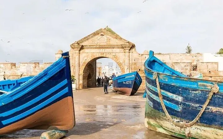 Essaouira harbor with blue fishing boats and historic stone gate, Marrakesh coastal tour.