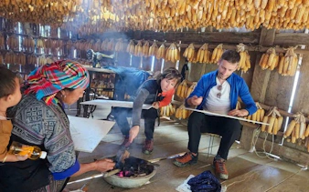 Local Hmong guide demonstrates traditional beeswax painting to tourists in Mu Cang Chai.