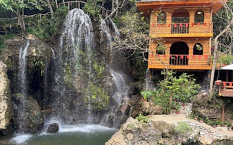 Waterfall beside wooden house in Sapa, Vietnam, part of guided drive and trek experience.