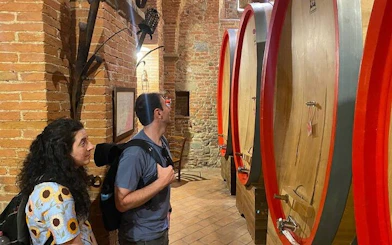 Visitors exploring wine barrels in a Tuscan winery cellar.