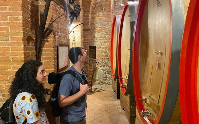 Visitors exploring wine barrels in a Tuscan winery cellar.