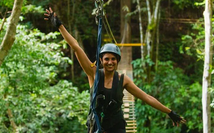 Person ziplining through rainforest at Braulio Carrillo, San Jose, with hanging bridge in background.