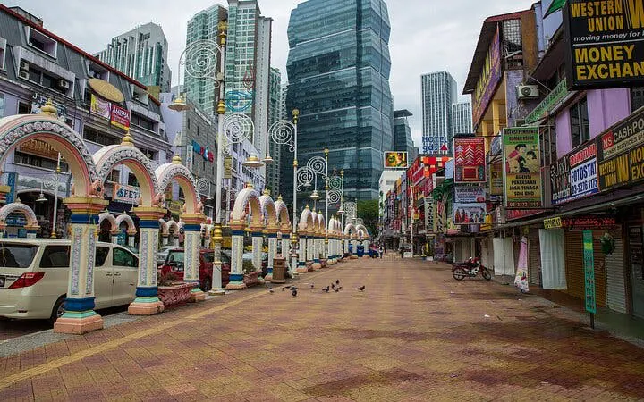 Street view in Kuala Lumpur with colorful arches and modern skyscrapers.