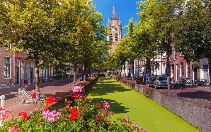 Delft canal with view of Nieuwe Kerk and vibrant flowers, part of Brussels to Keukenhof Gardens tour.