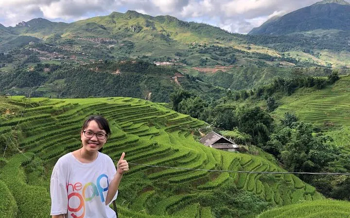 Sapa rice terraces with a person giving a thumbs up, showcasing lush green fields and distant mountains.