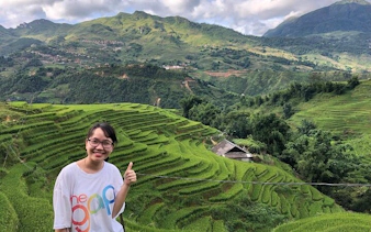 Sapa rice terraces with a person giving a thumbs up, showcasing lush green fields and distant mountains.
