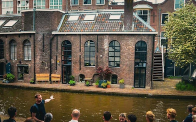 Local guide leading a small group by a canal in Utrecht, showcasing historic brick buildings.