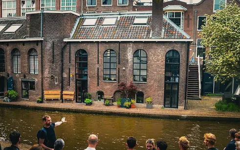 Local guide leading a small group by a canal in Utrecht, showcasing historic brick buildings.
