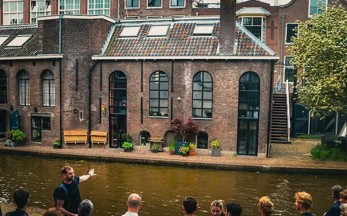 Local guide leading a small group by a canal in Utrecht, showcasing historic brick buildings.