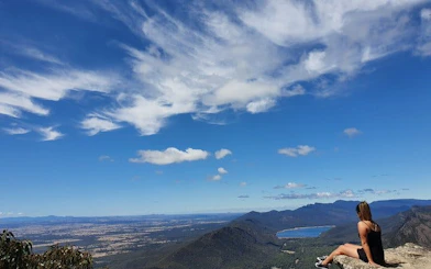 Hiker sitting on a rock overlooking Grampians National Park landscape and lake.