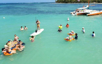 People enjoying snorkeling and paddleboarding near a catamaran in Punta Cana's natural reserve.